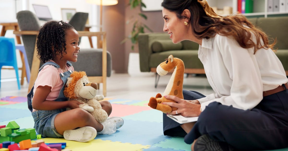 Child counsellor sitting on the floor at home with a young girl and her dolls during a warm in-home session