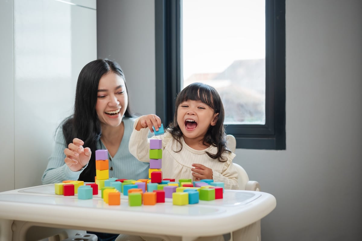 happy toddler girl playing wooden block toy cubes with her mother on a table