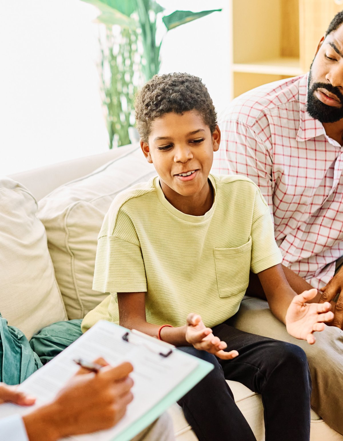 Father with his teenage son at a meeting with a counsellor, discussing mental health while sitting on a sofa in a warm, supportive office